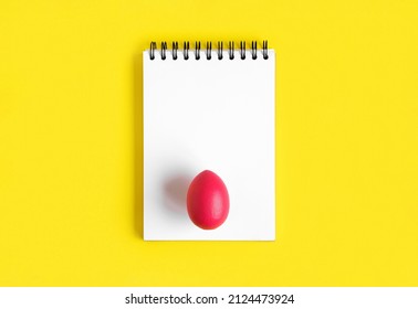 Notebook with red Easter Egg. Spiral notepad on spring yellow background. Top view of open writing pad with blank page, office flat lay. White Page for your write. Copy Space. Easter Mock Up.