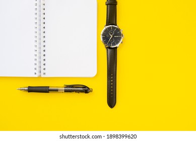 Notebook with ring binder with penand a wristwatch with leather straps, isolated on a yellow backdrop with copy space. Concept of writing and time.