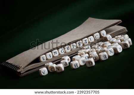 Notebook with spring and the word linguistics, made up of wooden cubes on a dark green. Concept of scientific research in linguistics and teaching linguistics at school or college. Photo. Close-up