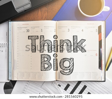 Notebook with text inside Think Big on table with coffee, laptop and some sheet of papers with charts and diagrams