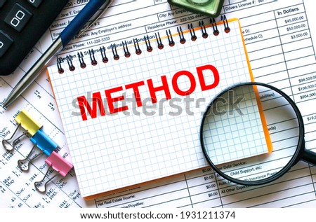 The notebook with the text Method lies on the financial tables with a calculator a magnifying glass a compass and paper clips. Financial concept