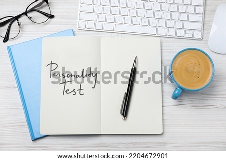 Notebook with text Personality Test, computer keyboard and cup of coffee on white wooden desk, flat lay