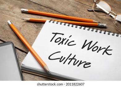 Notebook With Text Toxic Work Culture On Wooden Table, Closeup