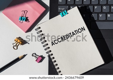 Notebook with tools and notes about ACCREDITATION lies on laptop.