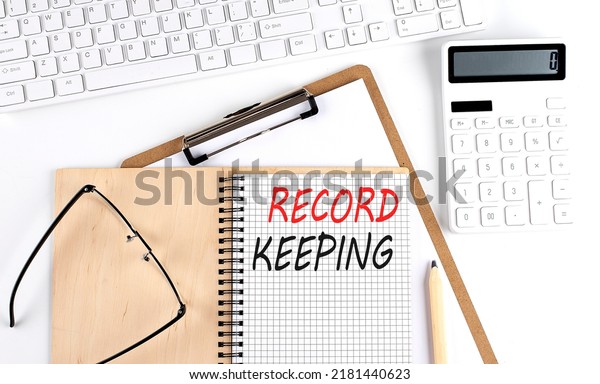 Notebook with the word RECORD KEEPING with\
keyboard and calculator on white\
background