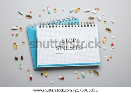 Notebook with word SINUSITIS surrounded by different pills on grey background, flat lay