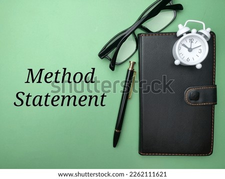 Notebook,clock and glasses with the word Method Statement on a green background.