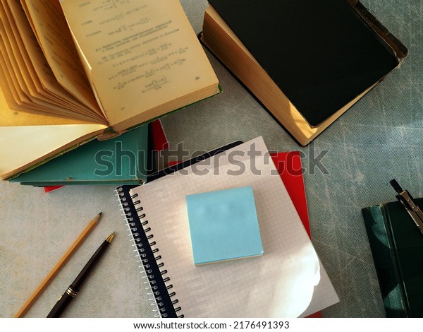 Notebooks and paper\
for notes are stacked. Books, pen, pencil, and compass are arranged\
around them in working order. The concept of scientific work,\
training, education.