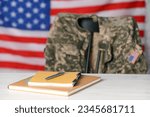 Notebooks and pen on white wooden table, chair with soldier uniform against flag of United States indoors. Military education