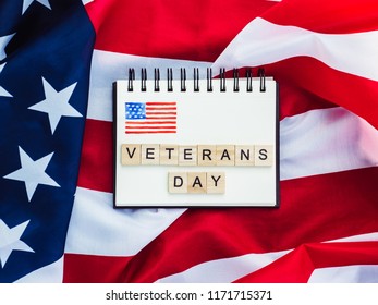 Notepad with blank page, wooden letters of the alphabet in the form of the words Veterans Day on the background of the US Flag. Top view, close-up - Shutterstock ID 1171715371