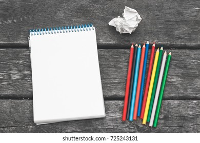 Notepad and blank sheet paper  colored pencils   crumpled sheet paper the old wooden background  Workplace the artist  writer  Never give up 