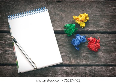 Notepad and blank sheet paper  pen   multicolored crumpled sheets paper the old wooden background  Workplace the artist  writer  Never give up 