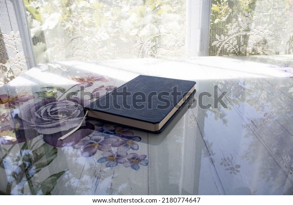 Notepad with blue cover placed on purple\
rose-patterned table.