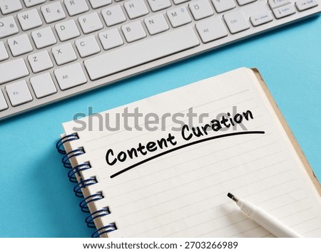 Notepad with content curation handwritten, keyboard, and pen on blue background represent organizing and presenting online information