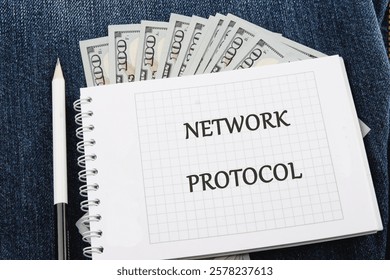 A notepad displaying the term network protocol rests nearby a fan of banknotes, illustrating the connection between technology concepts and financial aspects.