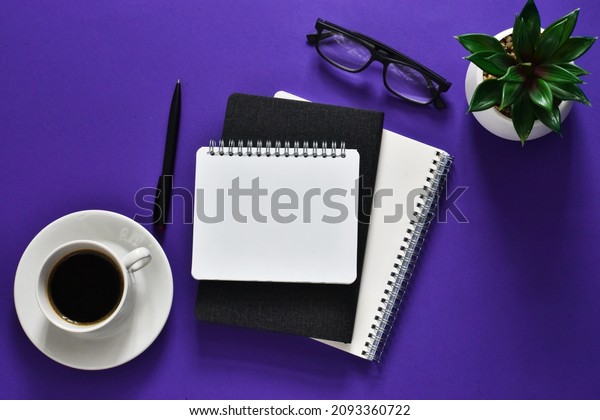 Notepad, green plant, eyeglasses with cup coffee\
and pen on violet background. Workplace. Office accessories. copy\
space, flat lay. Concept business and finance. Very peri - colors\
trend 2022 years
