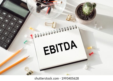 Notepad with inscriptions EBITDA - Earnings Before Interest, Taxes, Depreciation and Amortization, on a white office background.