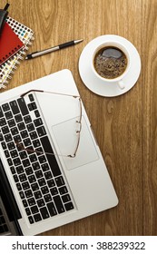 Notepad, Laptop, Spectacles And Coffee Cup On Wood Table. View From Above