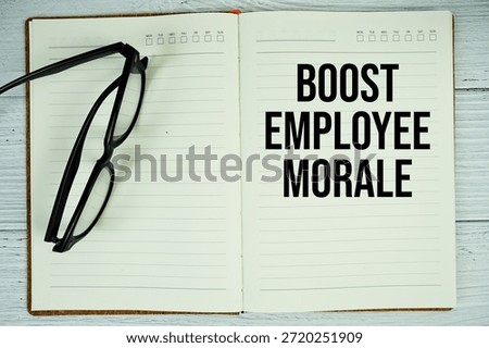 Notepad with message "Boost Employee Morale" and eyeglass on wooden background