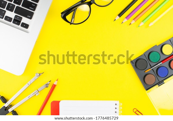 Notepad, multicolor pencils, divider, black\
glasses, colorful clips, oil colors for drawing and laptop on\
yellow background. Top view with copy space.\
