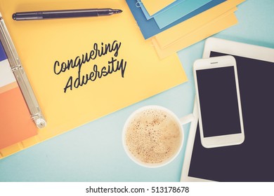 Notepad on workplace table and written CONQUERING ADVERSITY concept