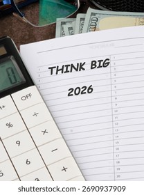 A notepad opened to display the words think big alongside a calculator and cash. The setup emphasizes planning for the future with a focus on the year 2026.