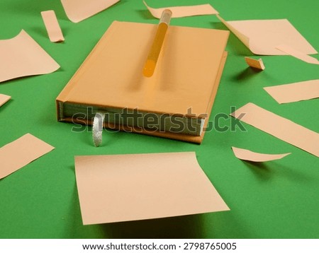 Notepad in orange binding, orange sticky notes and ballpoint pen lie on a green background. Objects for notations and diary.