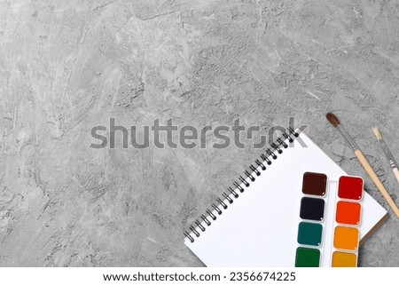 Notepad and paints on gray background, space for text