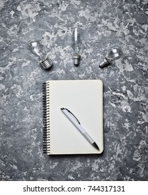 Notepad and pen on a concrete surface. Inspiration for the writer. Loft style. Workspace for ideas. Incandescent bulbs. Top view. Flat lay.