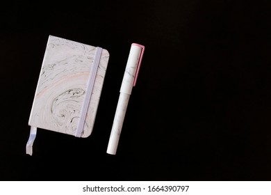 Notepad and pen with trendy marble pattern lie on black background flat lay. Picture with copy space