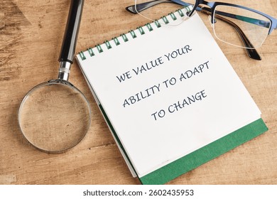 A notepad with the phrase about valuing adaptability lies on a wooden table next to a magnifying glass and a pair of glasses, highlighting the need for flexibility in life.