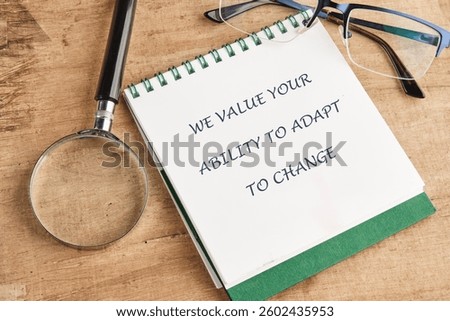 A notepad with the phrase about valuing adaptability lies on a wooden table next to a magnifying glass and a pair of glasses, highlighting the need for flexibility in life.