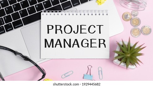 Notepad with PROJECT MANAGER text on keyboard with pencils, paper clips, potted flower.