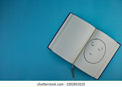 Notepad With Proud Emoji Placed On Blue Background.