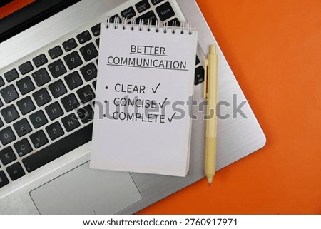 Notepad reading “Better Communication” with checklist items clear, concise and complete sits on a laptop keyboard beside a pen on orange background, conveying workplace communication and productivity.