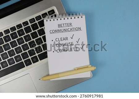 Notepad reading “Better Communication” with checklist items clear, concise and complete sits on a laptop keyboard beside a pen on blue background, conveying workplace communication and productivity.