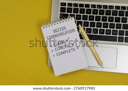 Notepad reading “Better Communication” with checklist items clear, concise and complete sits on a laptop keyboard beside a pen on yellow background, conveying workplace communication and productivity.