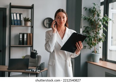 With Notepad And Smartphone In Hands. Young Beautiful Woman In Formal Clothes Is Working At Office.