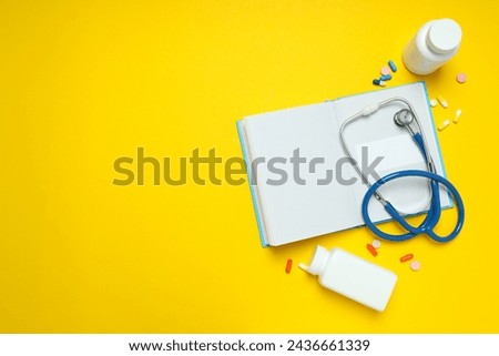 Notepad, stethoscope and jars of pills on yellow background, space for text