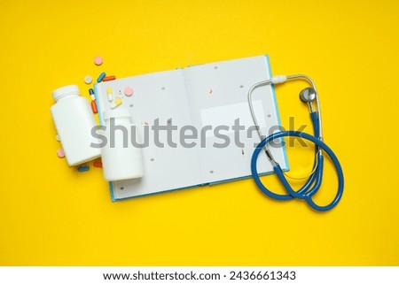 Notepad, stethoscope and jars of pills on yellow background, top view