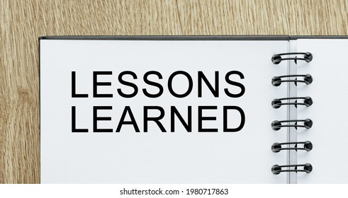 Notepad with text LESSONS LEARNED on wooden deskt. Business and finance concept