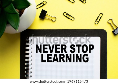 Notepad with text NEVER STOP LEARNING on the office desk with a plant, stationery. A blank notepad for entering a copy or text. Table with top view, flat yellow background concept. business