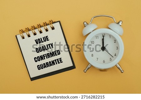 A notepad with text VALUE, QUALITY, CONFIRMED, GUARANTEE next to alarm clock against coloured background. Concept for business standards and timely service delivery