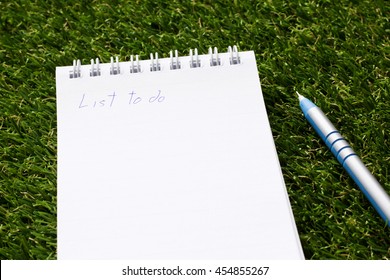 Notepad with wording list to do and pen on artificial green grass