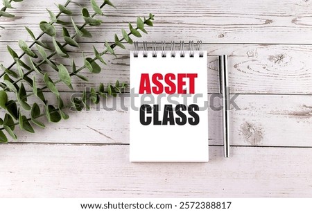 Notepad with the words asset class in bold red and black text on a white wooden background 
