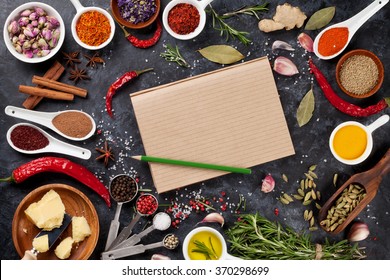 Notepad for your recipe with herbs and spices over black stone background. Top view with copy space