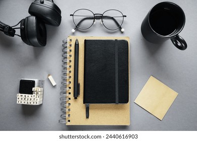 Notepads next to pen, sticky notes, cup of coffee, glasses, smartphone and headphones on gray background - Powered by Shutterstock