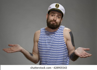 Nothing I Can Do. Shot Of A Bearded Sailor Hipster Looking Excusing To The Camera Spreading His Hands On Grey Background.