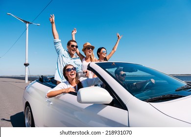 Nothing but friends and road ahead. Group of young happy people enjoying road trip in their white convertible and raising their arms up