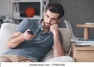 Nothing Interesting To Watch. Handsome Young Man Holding Remote Control And Looking Bored While Watching TV On The Couch At Home